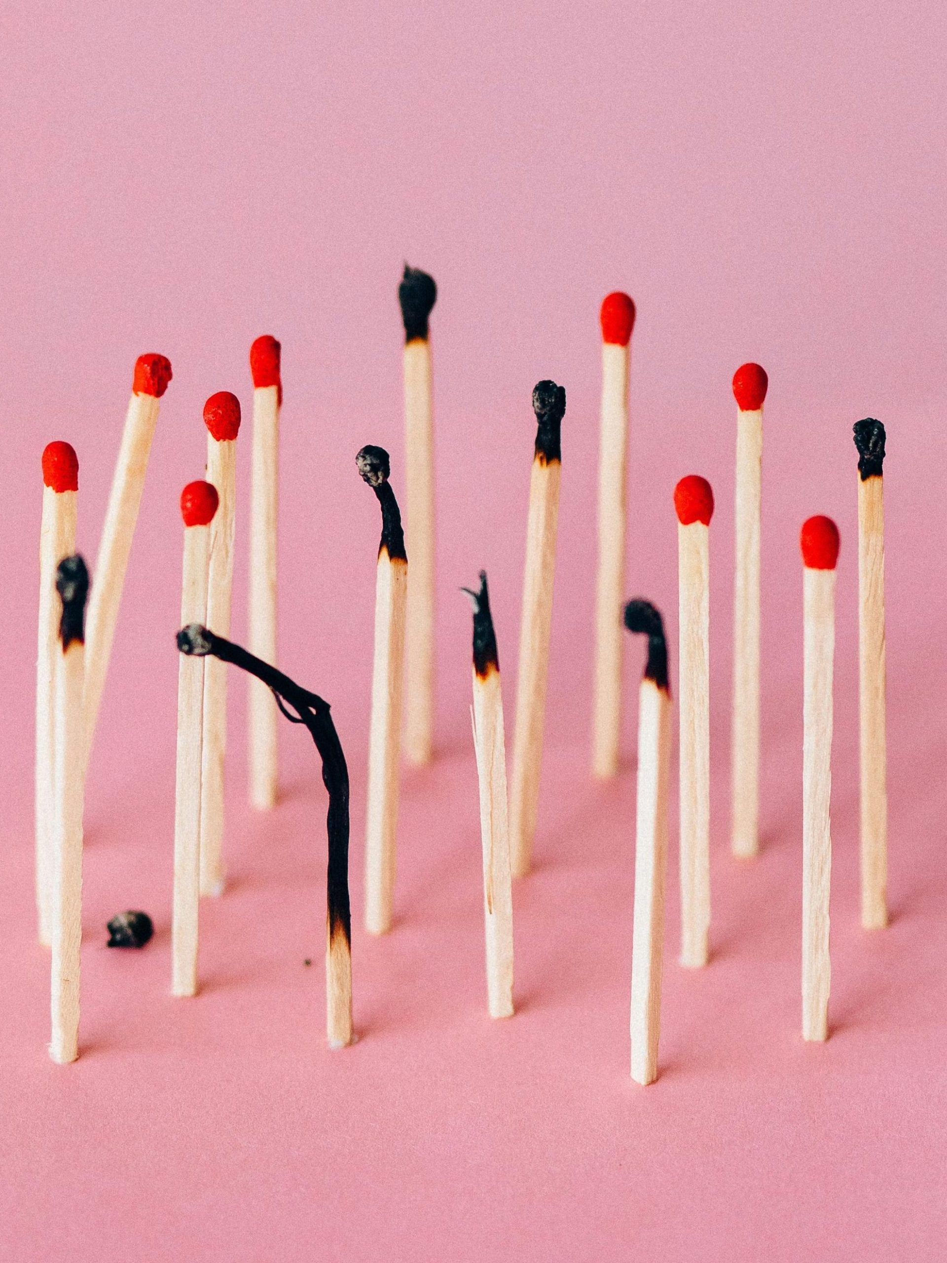 Artistic photo of burned matchsticks on pink background symbolizing burnout.